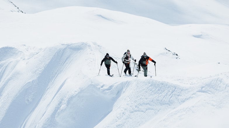 Drei Skitourengeher wandern auf einem schneebedeckten Grat in den Bergen.