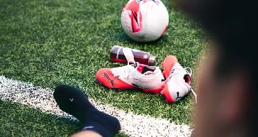Auf dem Rasen des Fußballfelds liegen ein Ball, eine Trinkflasche und ein Paar Fußballschuhe.