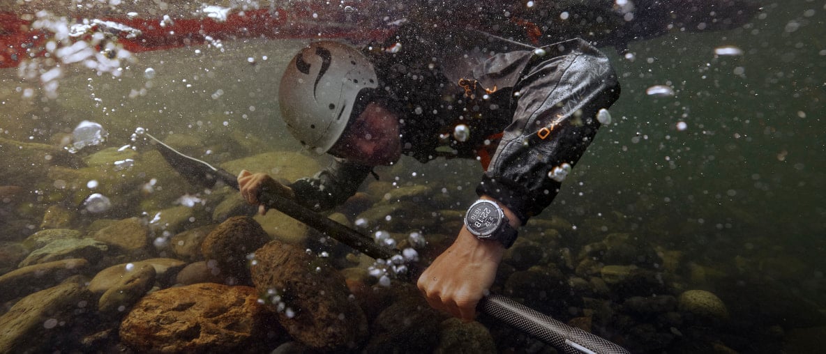 Ein Kajakfahrer unter Wasser mit Paddel, Helm und der Garmin Fenix 8 Pro am Handgelenk.
