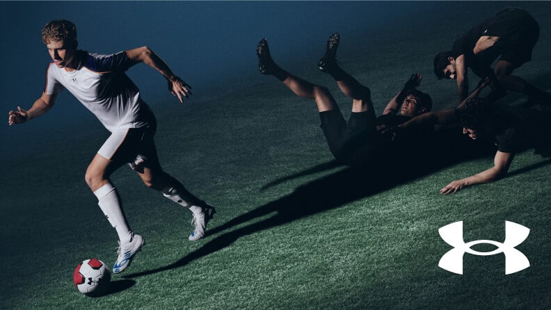 Ein Fußballer mit dem Under Armour Shadow Elite Fußballschuh und drei Fußballer die am Boden liegen und um den Ball kämpfen