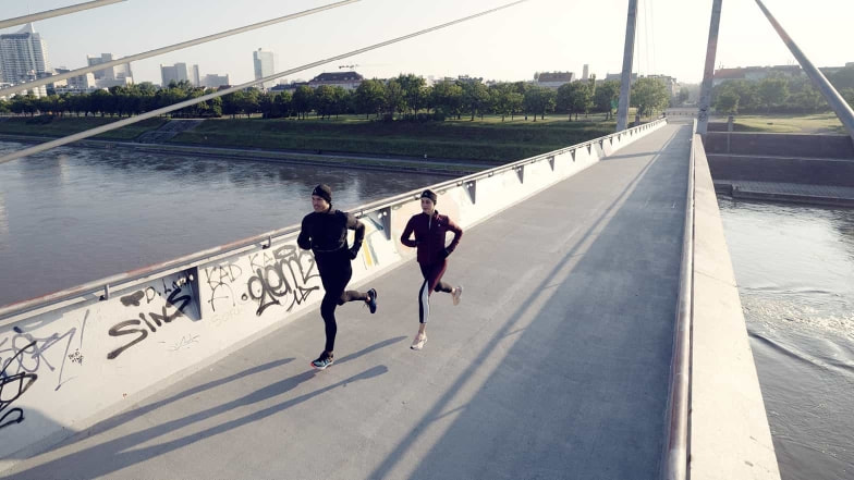 Eine Läuferin und ein Läufer laufen in den ruhigen Morgenstunden über eine Brücke in der Stadt.