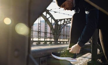 Eine Person in Sportkleidung bindet auf einer Brücke die Schnürsenkel ihres Laufschuhs.
