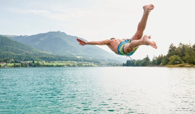 Schwimmer in Badehose der mit Kopfsprung in einen See hüpft