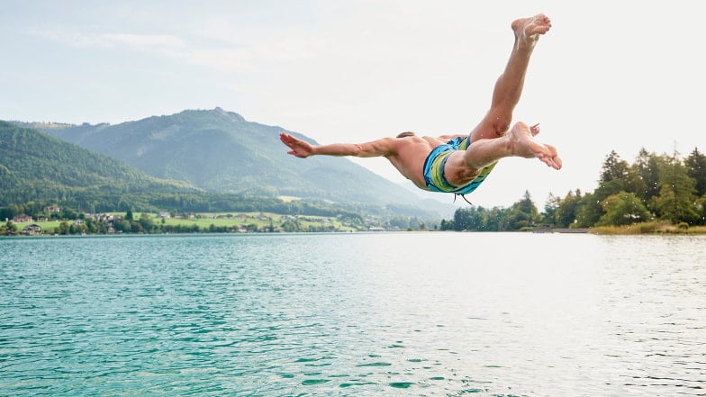 Schwimmer in Badehose der mit Kopfsprung in einen See hüpft