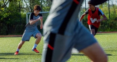 Mehrere jugendliche Fußballspieler laufen auf einem Kunstrasenplatz einem Ball hinterher. Zu sehen sind Spieler in Trainingskleidung während einer Spielsituation.