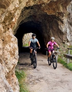 Zwei Radfahrer kommen auf einem Weg aus einem Felsentunnel.