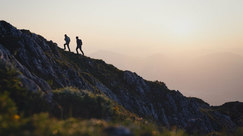 Zwei Wanderer besteigen einen steilen Berg bei Sonnenuntergang in den Alpen.