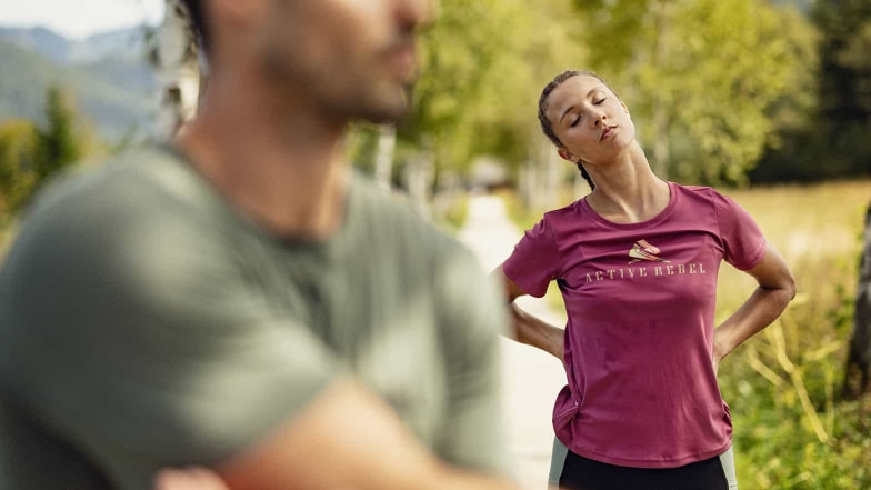 Eine Läuferin dehnt ihren Nacken nach einem gemütlichem Regenerationslauf. Ihr Laufpartner dehnt seine Schulterpartie.