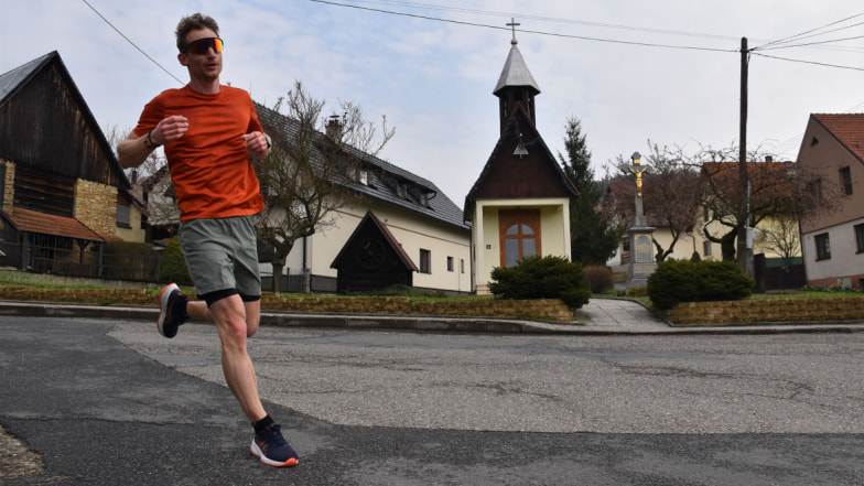 Běžec v oranžovém triku testuje boty Asics Gel Cumulus 27 na silnici.