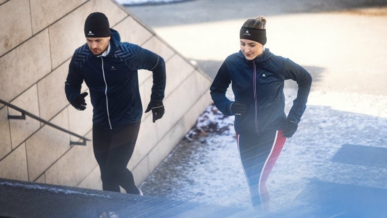 Mann und Frau joggen im Winter eine Treppe hinauf.