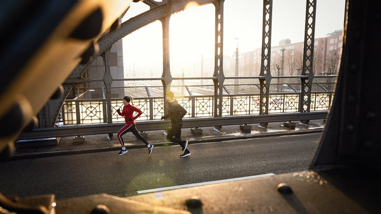 Zwei Personen laufen bei Sonnenaufgang über eine Brücke in der Stadt.
