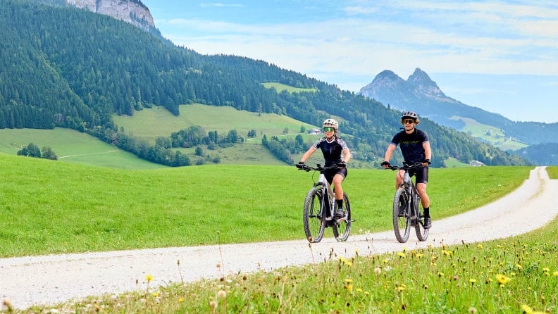 Paar beim Mountainbiken auf einem Schotterweg in den Bergen.