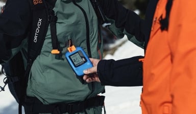 Zwei Personen machen einen Gruppen-Check mit einem Lawinensuchgerät im Schnee.