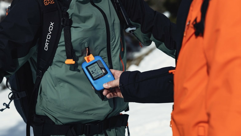 Zwei Personen machen einen Gruppen-Check mit einem Lawinensuchgerät im Schnee.