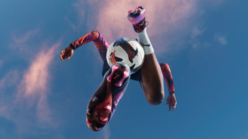 Fotbalista vyfocen zespodu ve skoku s detailem na Puma kopačky a Puma míč.