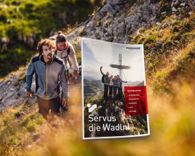 Titelblatt des INTERSPORT Outdoor-Special. Im Hintergrund ein Bild von einem Mann und einer Frau beim Aufstieg auf einen Berg durch eine Wiese.