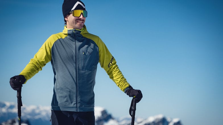 Ein lächelnder Mann mit Skistöcken in den verschneiten Bergen.