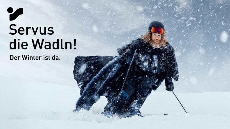 Der Winter (bärtiger Mann mit Pelzumhang) fährt Ski bei Schneefall.