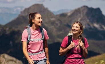 Zwei Frauen mit Rucksäcken wandern in den Bergen und unterhalten sich.