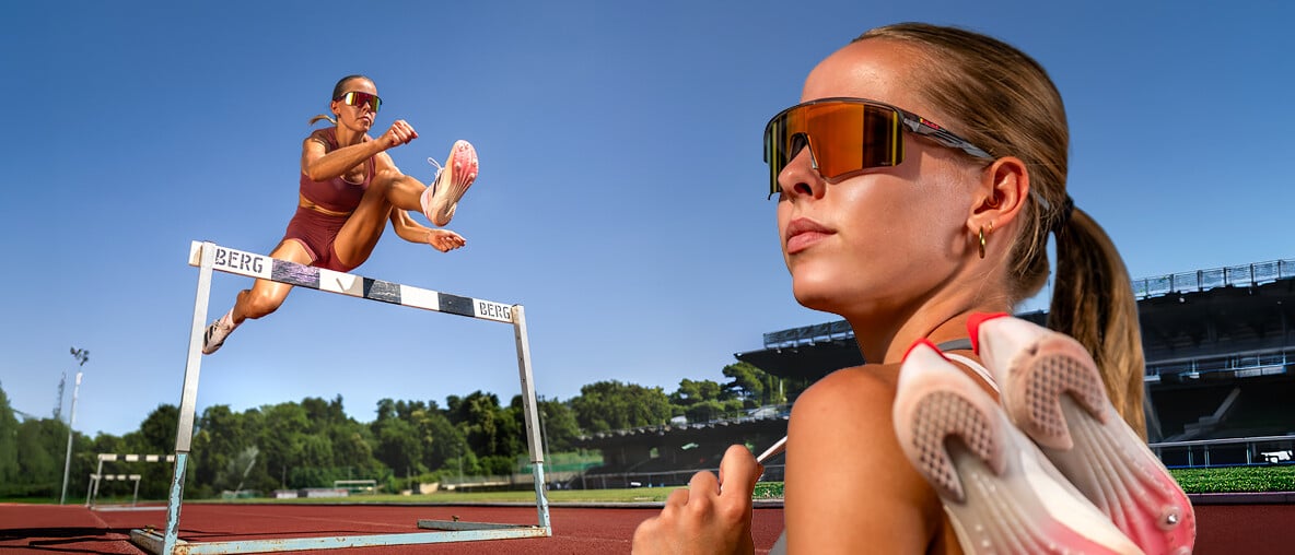 Leichtathletin überquert Hürde im Stadion, zweite Athletin mit Red Bull SPECT Brille und Spikes im Vordergrund.