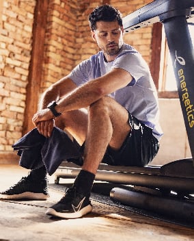 Mann dehnt sich sitzend auf einem Laufband in einem Fitnessraum
