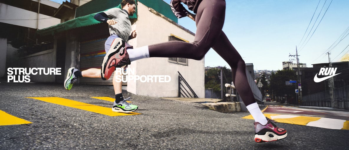 Zwei Läufer sprinten bergab durch die Stadt mit Nike Structure Plus für stabilen, unterstützten Straßenlauf