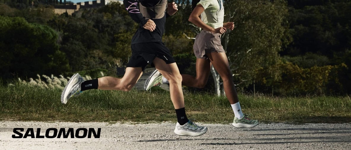 Zwei Läufer in Salomon-Ausrüstung rennen auf einem Schotterweg.
