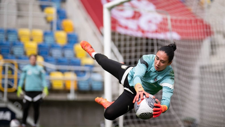 Eine Torhüterin hechtet im Training zur Seite und fängt den Fußball vor dem Tor, im Hintergrund ist eine weitere Spielerin zu sehen.