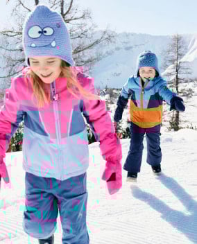Zwei Kinder spielen glücklich im Schnee vor einer Bergkulisse.