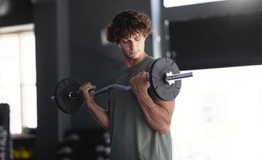 Mann trainiert im Fitnessstudio mit einer Langhantel und führt eine Bizepsübung aus.