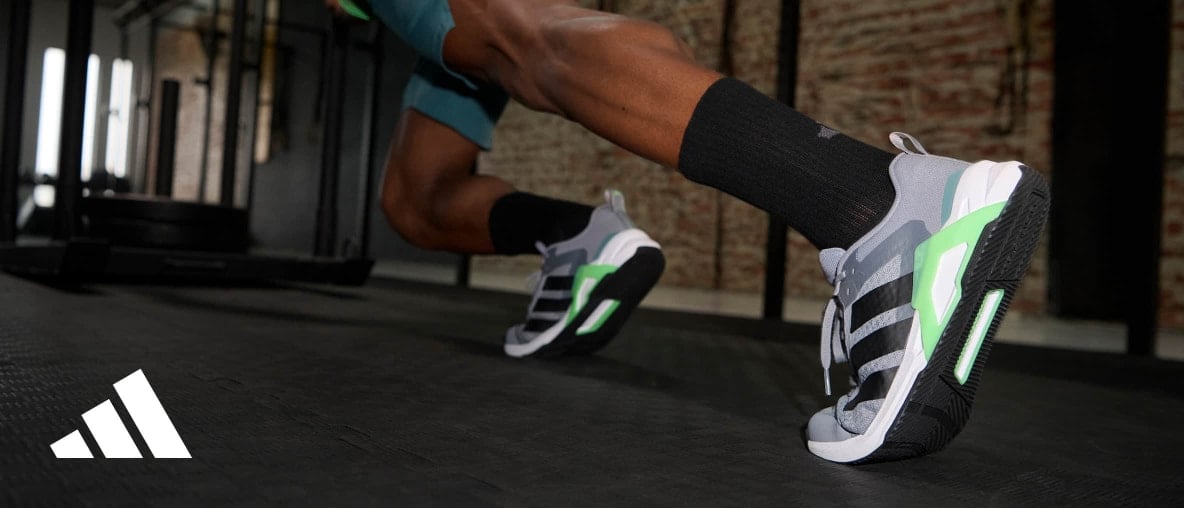 Nahaufnahme von sportlichen Laufschuhen mit grauen, schwarzen und grünen Elementen auf einem Trainingsboden in einem Fitnessstudio.