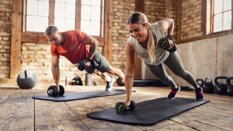 Ein Paar trainiert gemeinsam Kraftsport mit Hanteln in einem Studio.