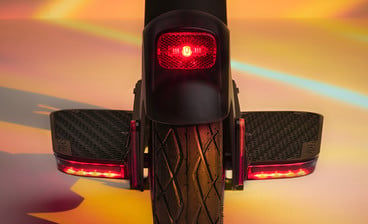 PURE E-Scooter von hinten mit leuchtenden roten Rücklichtern und integrierten Blinkern bei Sonnenuntergang