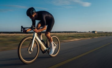 Rennradfahrer mit Met Fahrradhelm auf weißem Rennrad auf der einer langen Straße