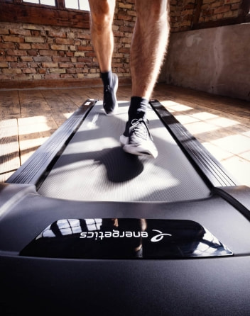 Nahaufnahme von Beinen auf einem Laufband in einem Fitnessraum mit Backsteinwänden.