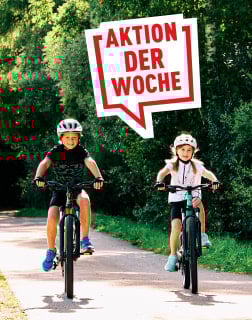 Zwei Kinder fahren mit Helmen Fahrrad auf einem sonnigen Weg.