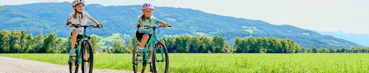 Zwei Mädchen fahren Fahrrad auf einem Weg in den Bergen.