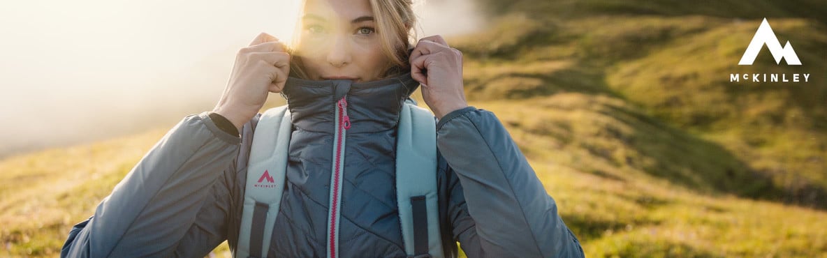 Eine Frau in den Bergen mit Outdoorbekleidung und -ausrüstung von McKINLEY.