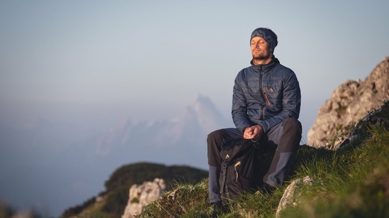 Ein Mann genießt mit geschlossenen Augen auf einem Berg die Morgensonne.