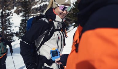 Personen überprüfen ein Lawinensuchgerät bei einer Skitour im Schnee.