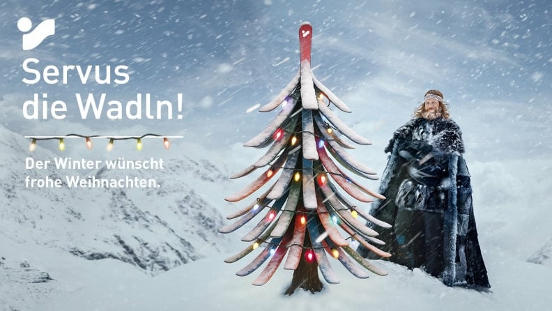 Der Winter wünscht frohe Weihnachten. Er steht neben einem Weihnachtsbaum, der aus Skiern gebastelt wurde.