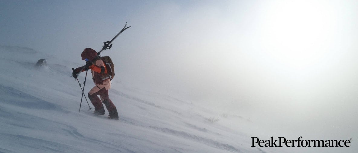 Eine Person mit Skiern besteigt einen Berg im dichten Schneetreiben.