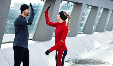 Mann und Frau in Laufbekleidung geben sich ein High-Five nach dem erfolgreichen Trainingslauf.