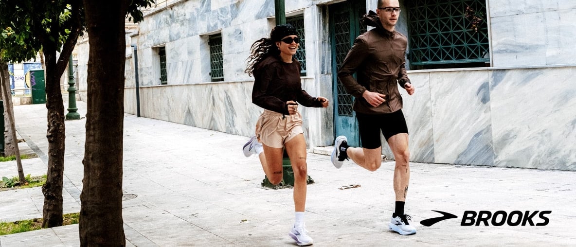 Eine Läuferin und ein Läufer laufen durch eine Stadt mit Brooks Ghost 18 Laufschuhen.