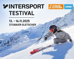 Eine Skifahrerin fährt auf roten Atomic-Skiern eine frisch präparierte Piste hinab, im Hintergrund schneebedeckte Berge.