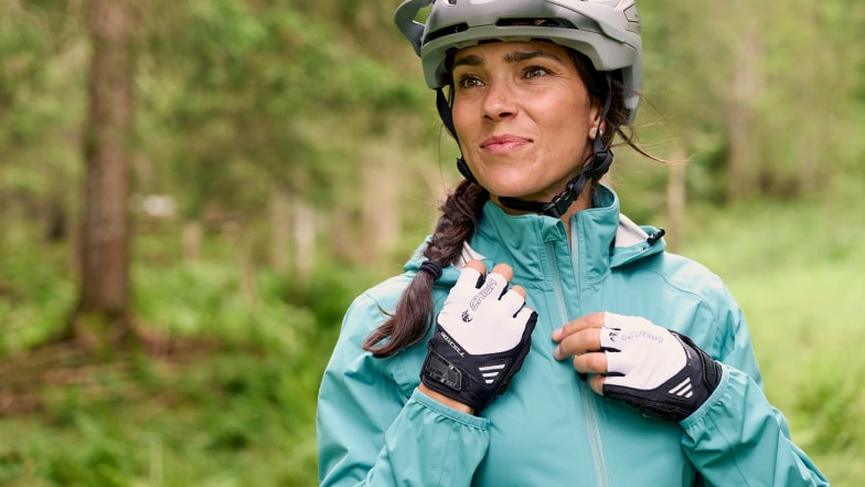 Eine Radfahrerin mit Helm und Handschuhen in einem grünen Wald.