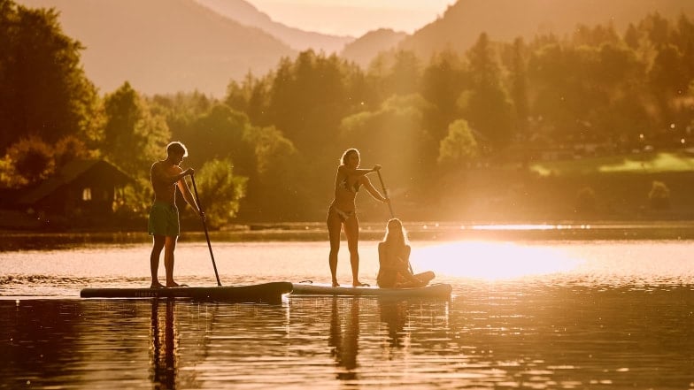 Eine Gruppe von Menschen mit SUPs auf einem See bei untergehender Sonne.