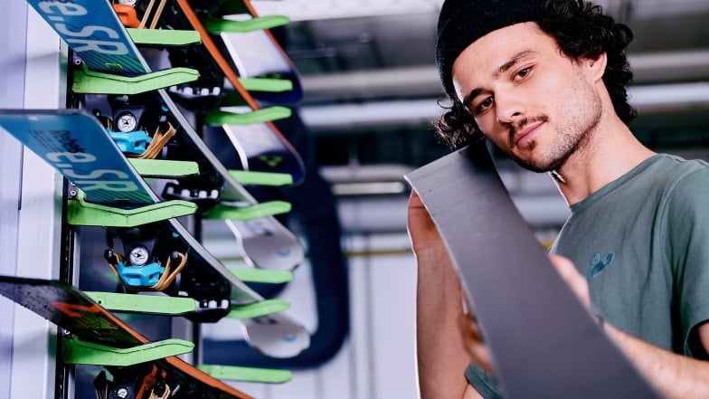 Ein junger INTERSPORT Mitarbeiter serviciert in einer Skiwerkstatt Skiern.