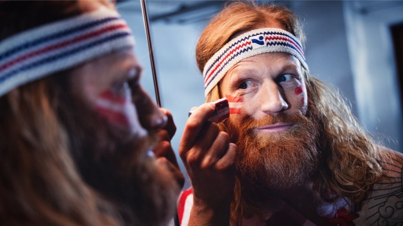 Österreich-Fan trägt rot-weiße Fan-Schminke vor dem Spiegel auf und bereitet sich auf das nächste ÖFB-Spiel vor.