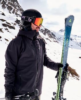 Skifahrer mit Helm, Skibrille und Fischer-Skiern vor verschneitem Bergpanorama
